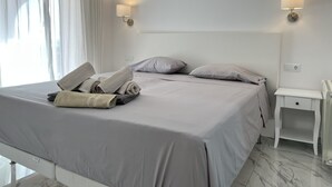 Un lit bien fait, agrémenté de serviettes, une table de chevet et des lampes fixées au mur, dans une chambre d’hôtel moderne.
