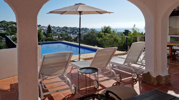 Un espace piscine comprenant deux chaises longues et un parasol, offrant une vue panoramique sur la mer et la ville.