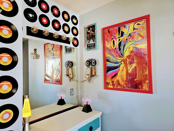 Una stanza con una parete decorata da dischi in vinile, uno specchio e un grande poster di Janis Joplin.