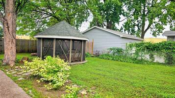 A gazebo with a screened porch, surrounded by a well-maintained lawn and a wooden fence.