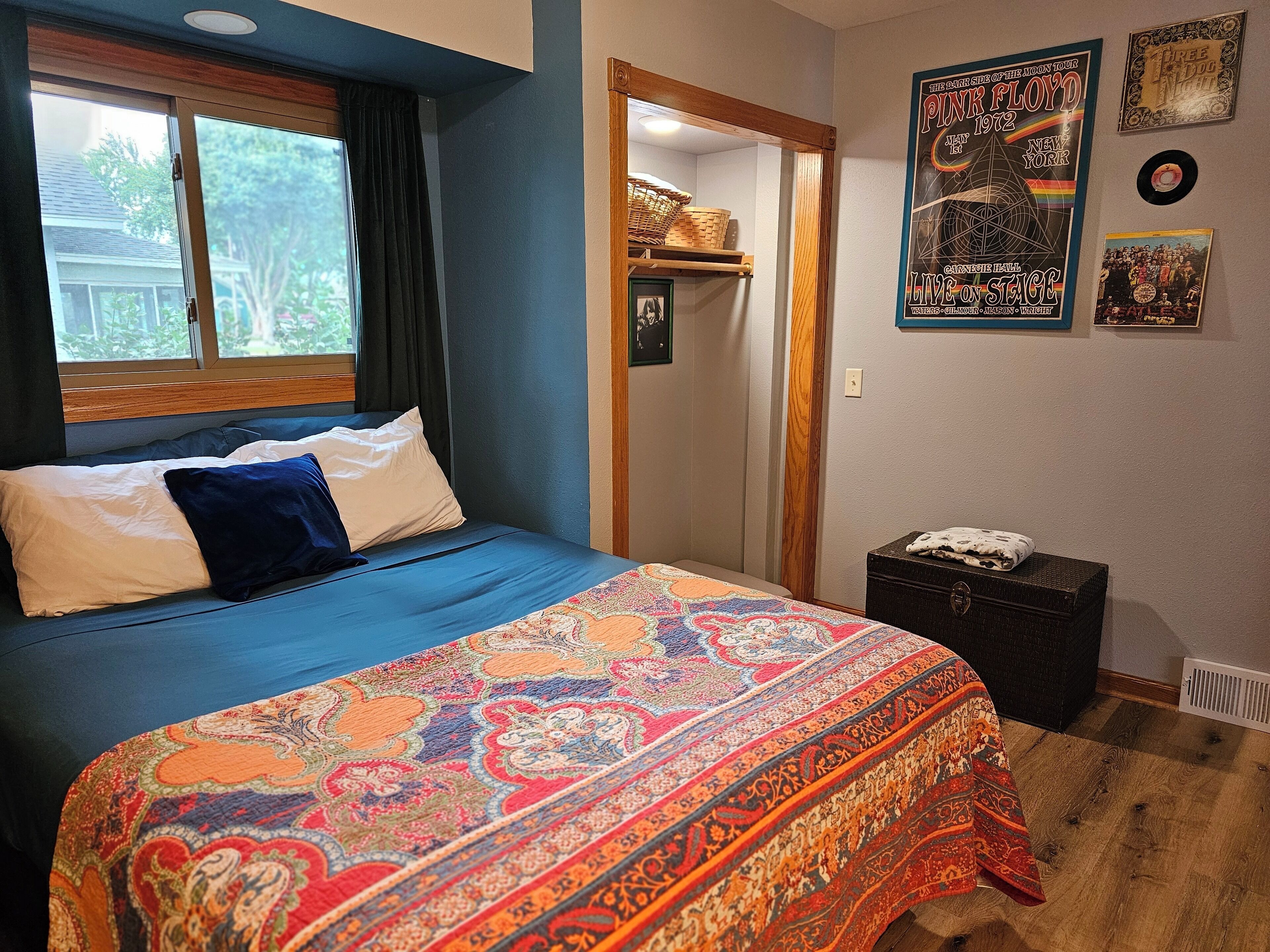 Ein Schlafzimmer mit einem großen Bett, einem Fenster, einer Tür und einer Wand mit Postern und Schallplatten.