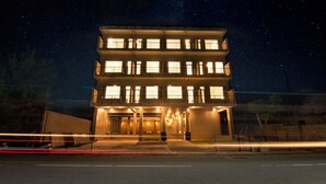 Um hotel com vários andares, janelas iluminadas e uma entrada central.