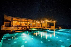 A nighttime swimming pool with a starry sky, a building with illuminated windows, and a well-lit deck area. - somerset mirissa blue (Mirissa)