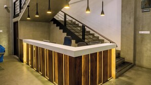 Bancada de recepção com acabamento em madeira, escada e iluminação pendente.