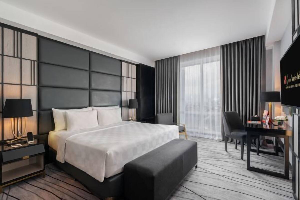Una habitación de hotel moderna con una cama grande, un escritorio con silla, una mesita de noche y un televisor.