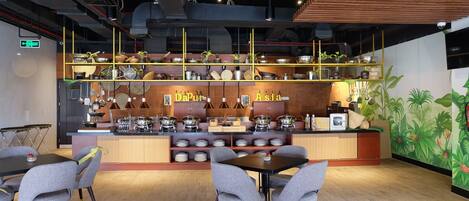 Un restaurante con mostrador de madera, varias estaciones de cocina y una zona de estar con mesas y sillas.