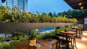 Een terras met tafels en stoelen, een betonnen plantenbak met beplanting, en uitzicht op zee.