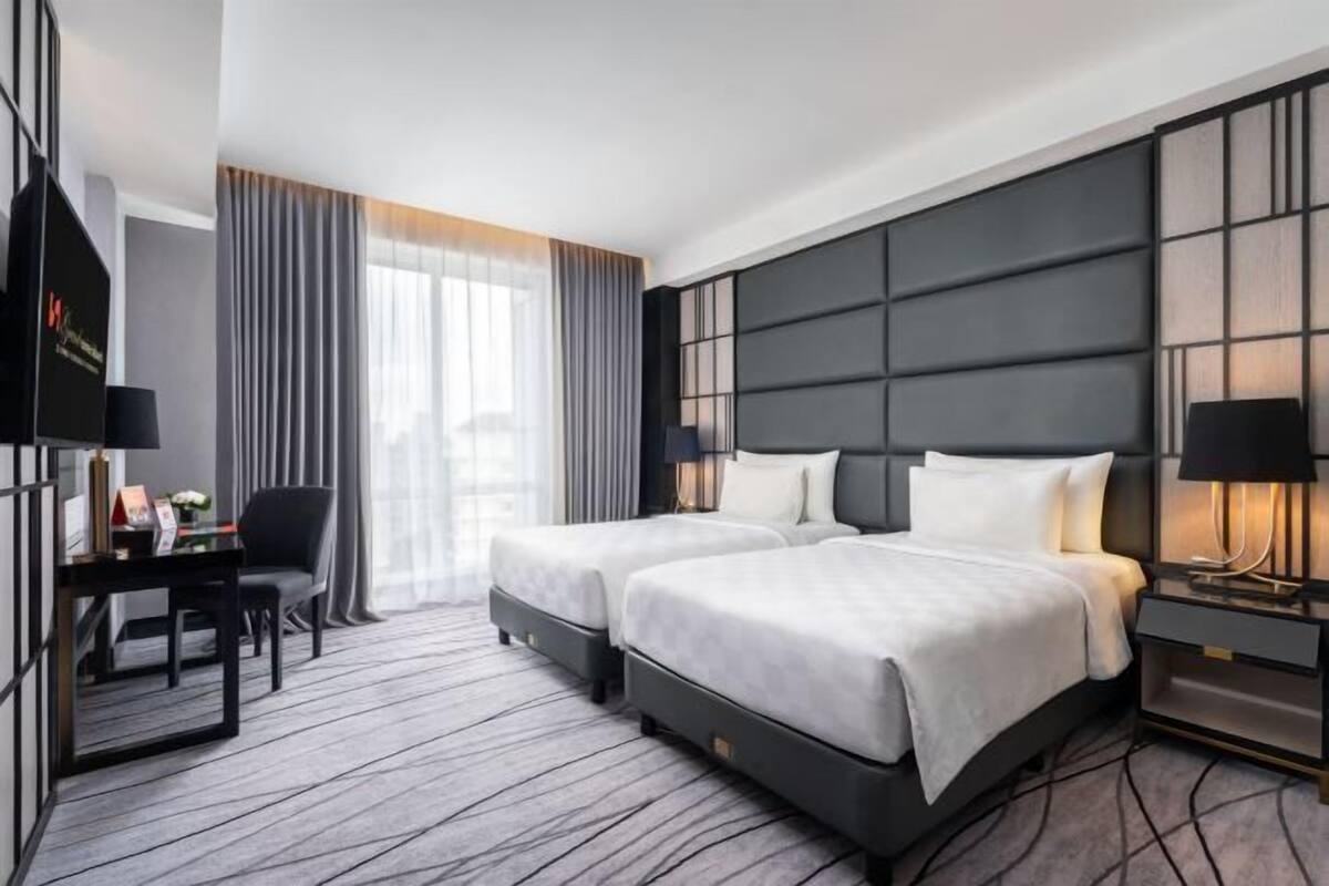 Habitación de hotel con dos camas, un escritorio, una silla y un ventanal con cortinas.