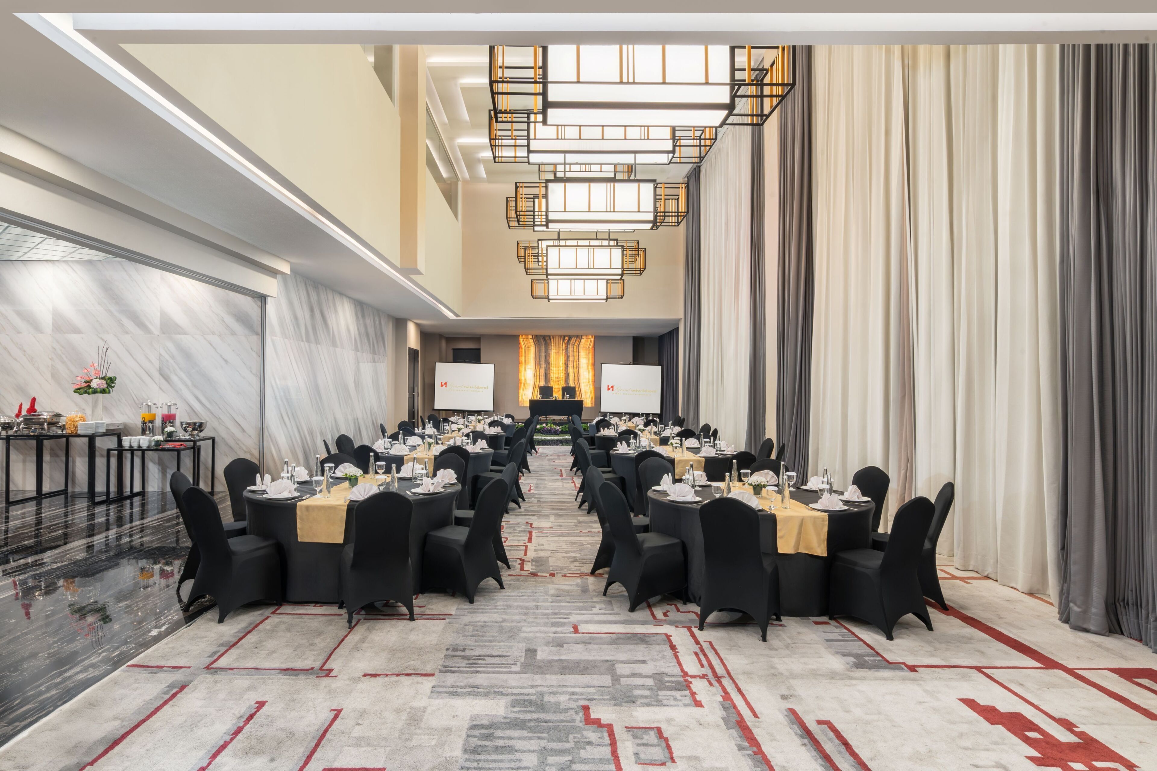 A conference room with tables and chairs arranged for a meeting, a large screen at the front, and a chandelier.