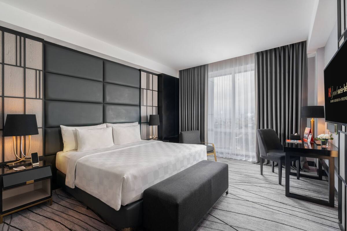 Una habitación de hotel moderna con una cama grande, un escritorio con una silla, un televisor y vistas a la ciudad.