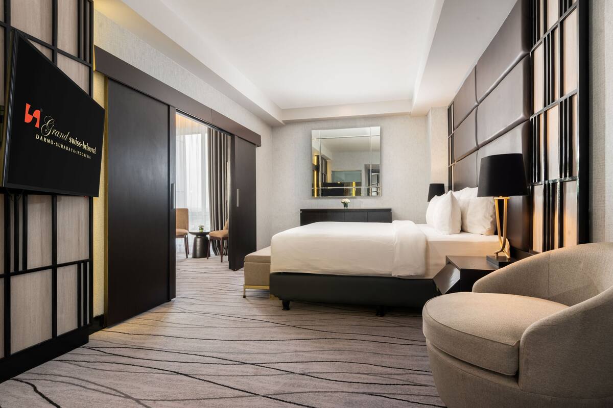 Habitación de hotel con cama, una silla, un escritorio, un espejo y televisión montada en la pared.