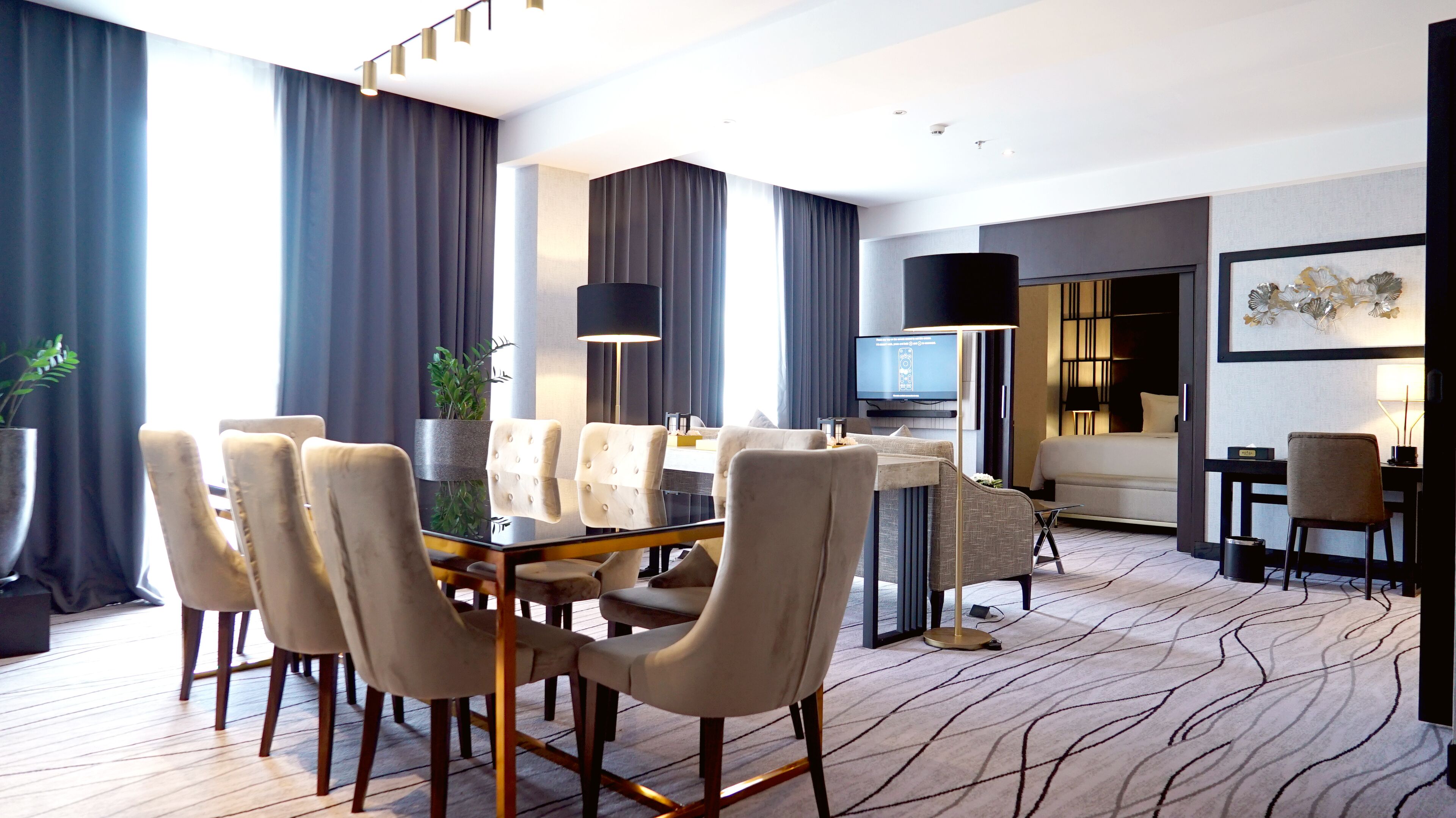 Une chambre d’hôtel moderne dotée d’un coin repas, d’un canapé, d’une télévision et d’une grande fenêtre avec des rideaux.