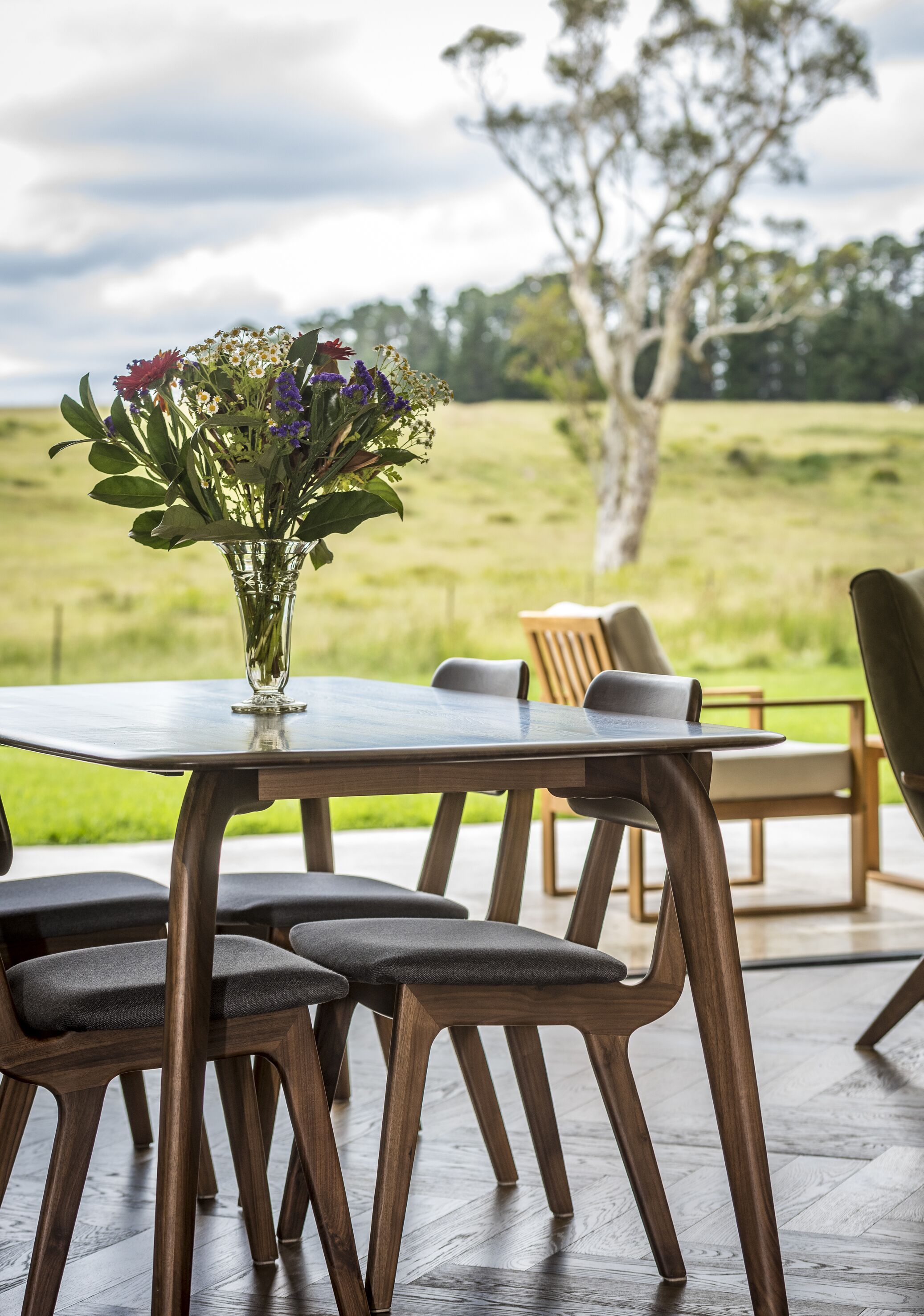 Uma mesa de jantar com cadeiras, um vaso com flores e vista para um campo gramado.