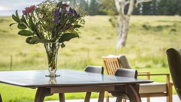 Uma mesa de jantar com cadeiras, um vaso com flores e vista para um campo gramado.