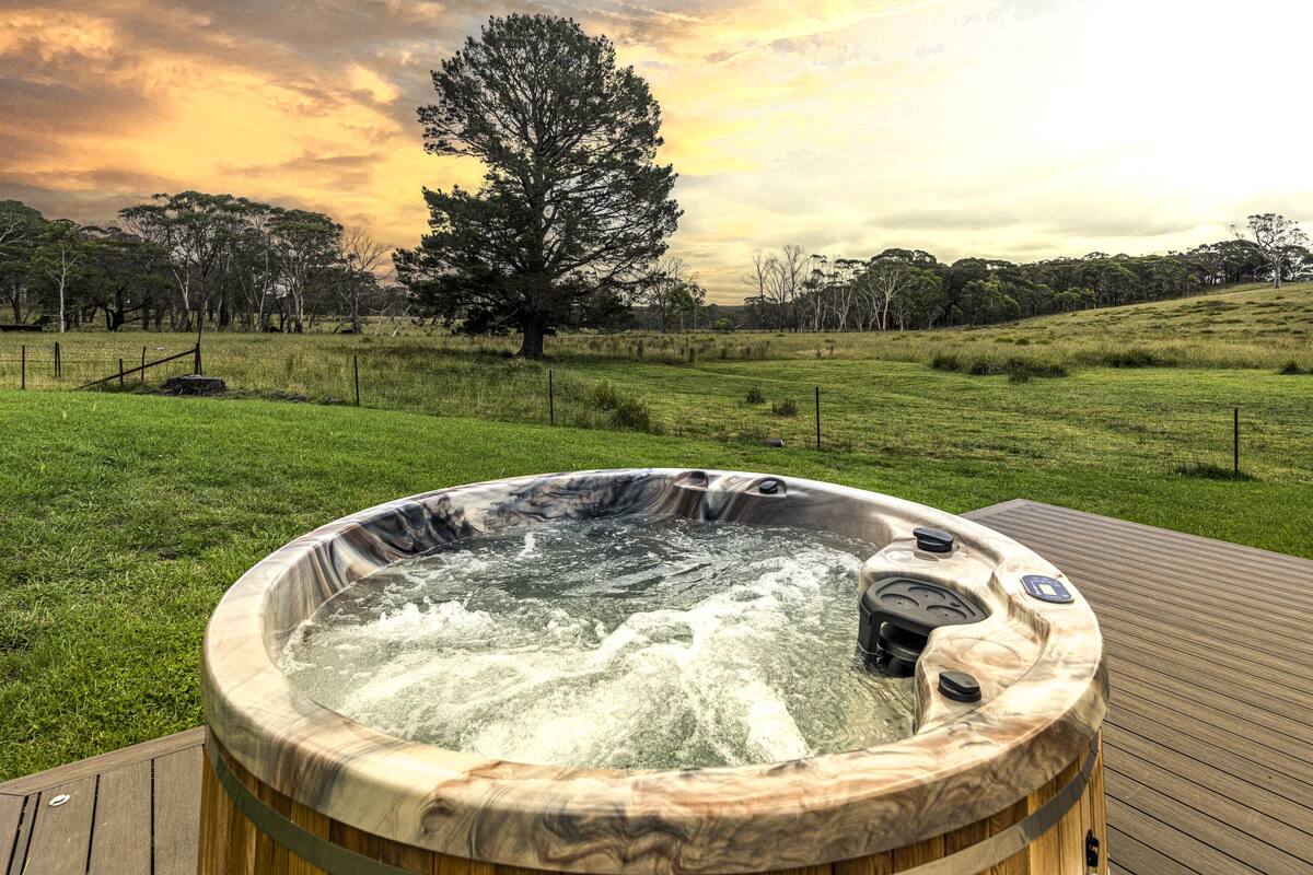 A hot tub on a wooden deck with a grassy field and trees in the background.