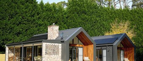 A modern house with a large glass facade, a brick chimney, and a sloped roof.