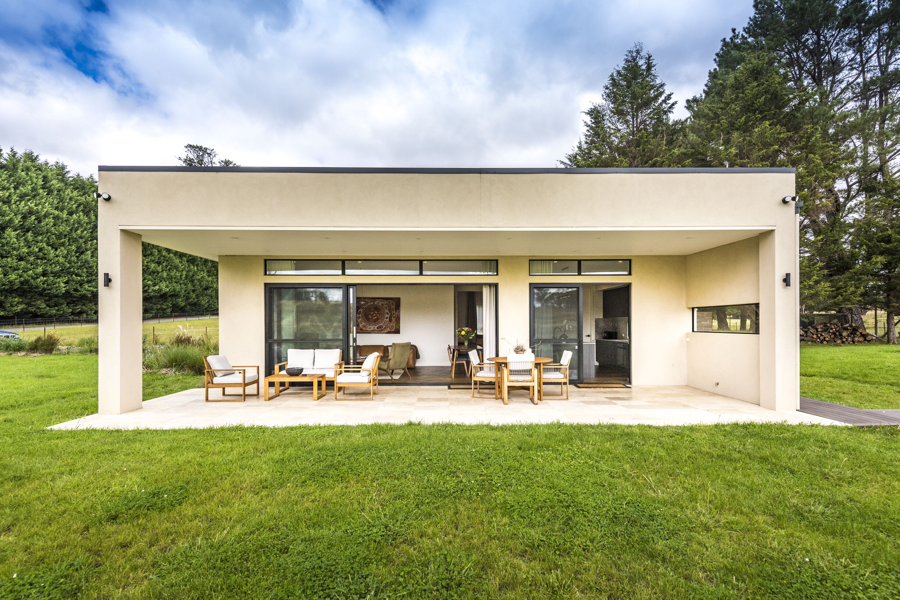 A modern house with a covered patio, large windows, and a lawn.