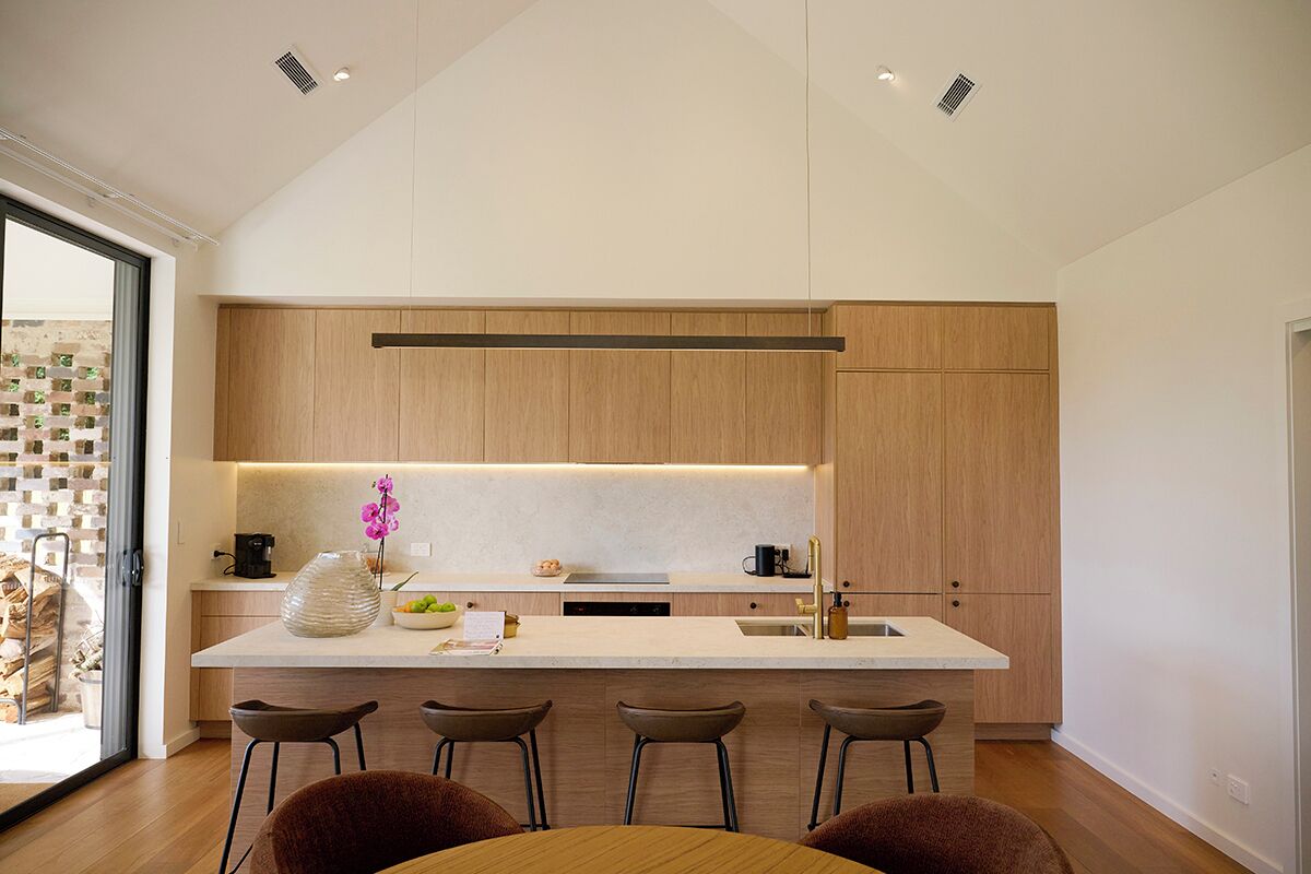 A modern kitchen with a central island, bar stools, and a view of a brick wall.