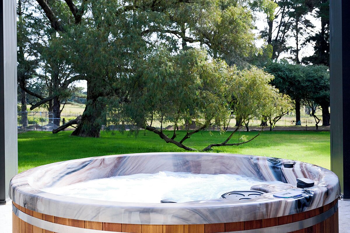 A hot tub with a wooden exterior, surrounded by trees and a grassy area.