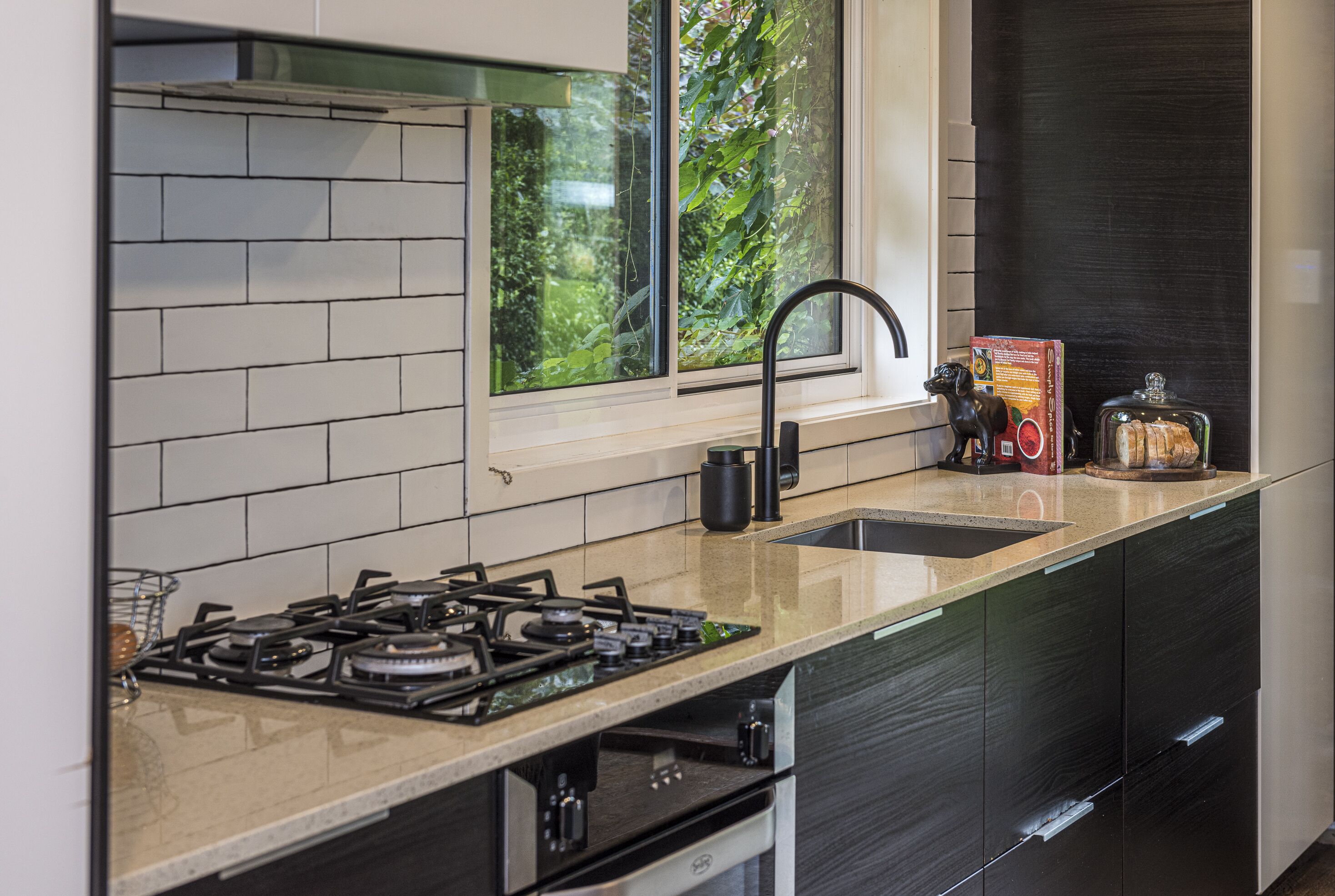 A modern kitchen with a gas stove, a sink, and a window with a view of greenery.