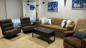 Una sala de estar con un sofá marrón, dos sillones, una mesa de centro y un televisor. Hay dos cuadros colgados en la pared y una lámpara de pie.
