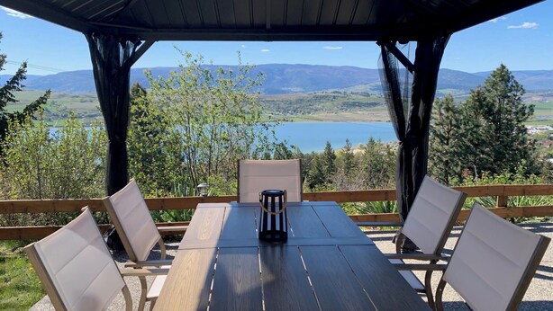 Una mesa de madera con sillas, un farol y vistas a un lago y montañas.
