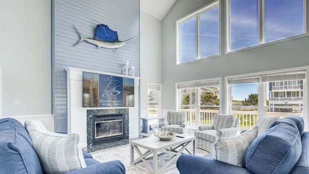A spacious living room with a fireplace, comfortable seating, and large windows offering a view of the outdoors.
