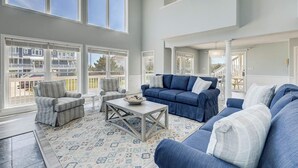 A spacious living room with large windows, a blue sofa set, and a patterned rug.