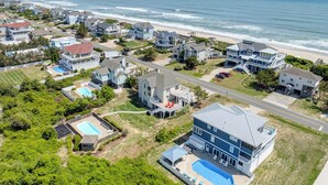 A coastal residential area with houses, a large swimming pool, and a beach in the background.