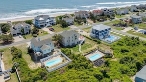 A coastal residential area with houses, a swimming pool, and a beach in the background.
