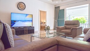 A modern living room with a flat-screen TV, a glass coffee table, and a beige sofa. - 6 Bedroom Tropical Pool Villa - V6 (Pattaya)