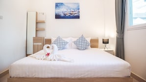 A neatly made bed with white linens and decorative pillows, a bedside table with a lamp, a wall-mounted air conditioner, and a framed picture of a snowy landscape. - 6 Bedroom Tropical Pool Villa - V6 (Pattaya)