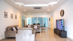 A spacious living room with a modern design, featuring a large flat-screen TV, leather sofas, and a minimalist decor. - 6 Bedroom Tropical Pool Villa - V6 (Pattaya)