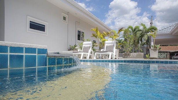 A swimming pool with a tiled edge, white lounge chairs, and a small waterfall feature. - 6 Bedroom Tropical Pool Villa - V6 (Pattaya)