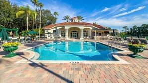 A swimming pool with lounge chairs and umbrellas, surrounded by a building with a tiled roof.