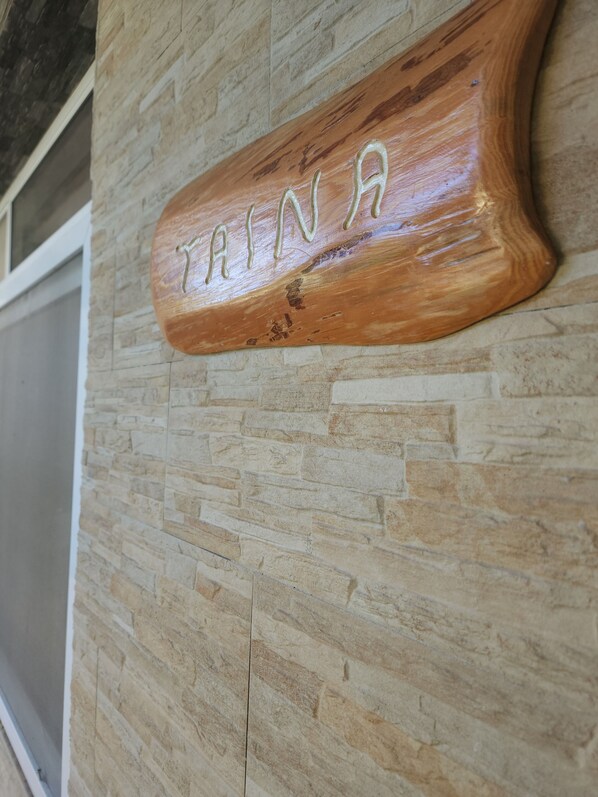 A wooden sign with the name "TRINA" carved into it, mounted on a stone wall. - Taina - Grand Appartement Avec Terrasse Avec Accès mer (AVERA - TAPUTAPUATEA)