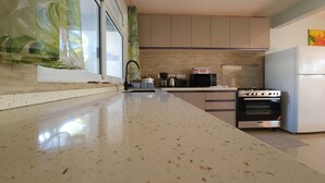 A kitchen with a large countertop, a stove, a microwave, and a refrigerator. - Taina - Grand Appartement Avec Terrasse Avec Accès mer (AVERA - TAPUTAPUATEA)
