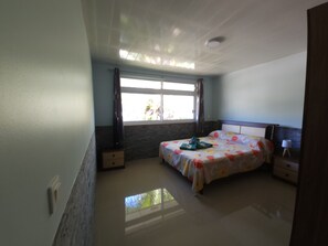 A bedroom with a bed, a nightstand, a lamp, a window, and a ceiling light.