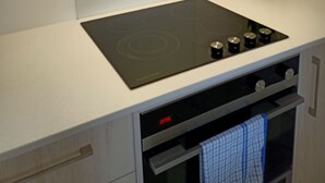 Ett modernt kök med en svart induktionshäll, en inbyggd ugn och en rostfri köksfläkt.
