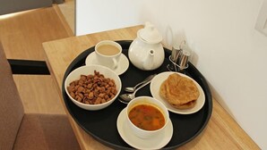 Una bandeja con una taza de café, una tetera, un bol de sopa, una fuente de pan plano y un bol de cereal.