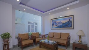 Una sala moderna con sofá, dos sillones, una mesa de centro y una lámpara. Hay un cuadro en la pared y una planta en maceta sobre una mesita auxiliar.