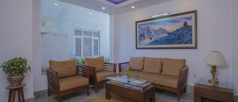 A modern living room with a sofa, two armchairs, a coffee table, and a lamp. There is a painting on the wall and a potted plant on a side table.