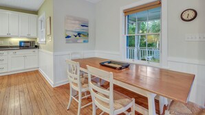 A kitchen with white cabinets, a wooden dining table, and a window with a view of greenery. - Relaxing Getaway w/ Private Pool (Tybee Island)