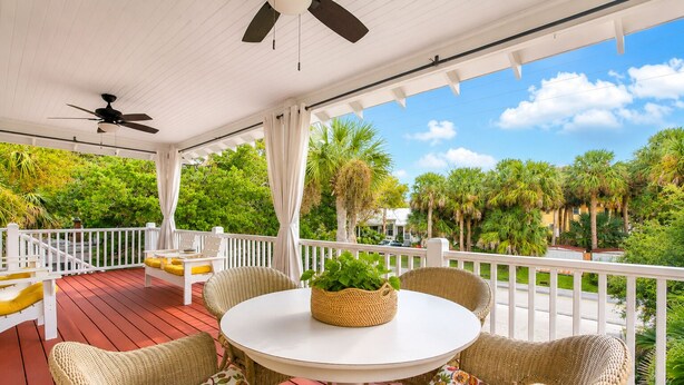A covered outdoor area with wicker furniture, a table with a plant, and a view of palm trees and greenery. - Relaxing Getaway w/ Private Pool (Tybee Island)