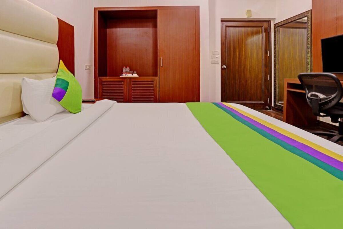 A hotel room with a bed, a wooden wardrobe, a desk, and a chair.