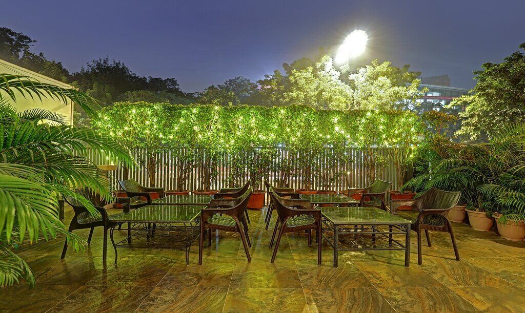An outdoor seating area with tables and chairs, surrounded by potted plants and a decorative fence with lights.