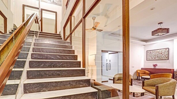 A modern interior with a marble staircase, a glass door leading to a room, and a seating area with leather chairs. - Hotel Bel Morris (New Delhi)