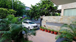 A white car parked in a driveway with potted plants and a stone wall. - Hotel Bel Morris (New Delhi)