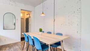 Ein Essbereich mit einem Holztisch, blauen Stühlen, einer Pendelleuchte und einer weißen Ziegelwand.