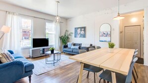 Ein modernes Wohnzimmer mit Sofa, Fernseher, Esstisch und Pflanzen.
